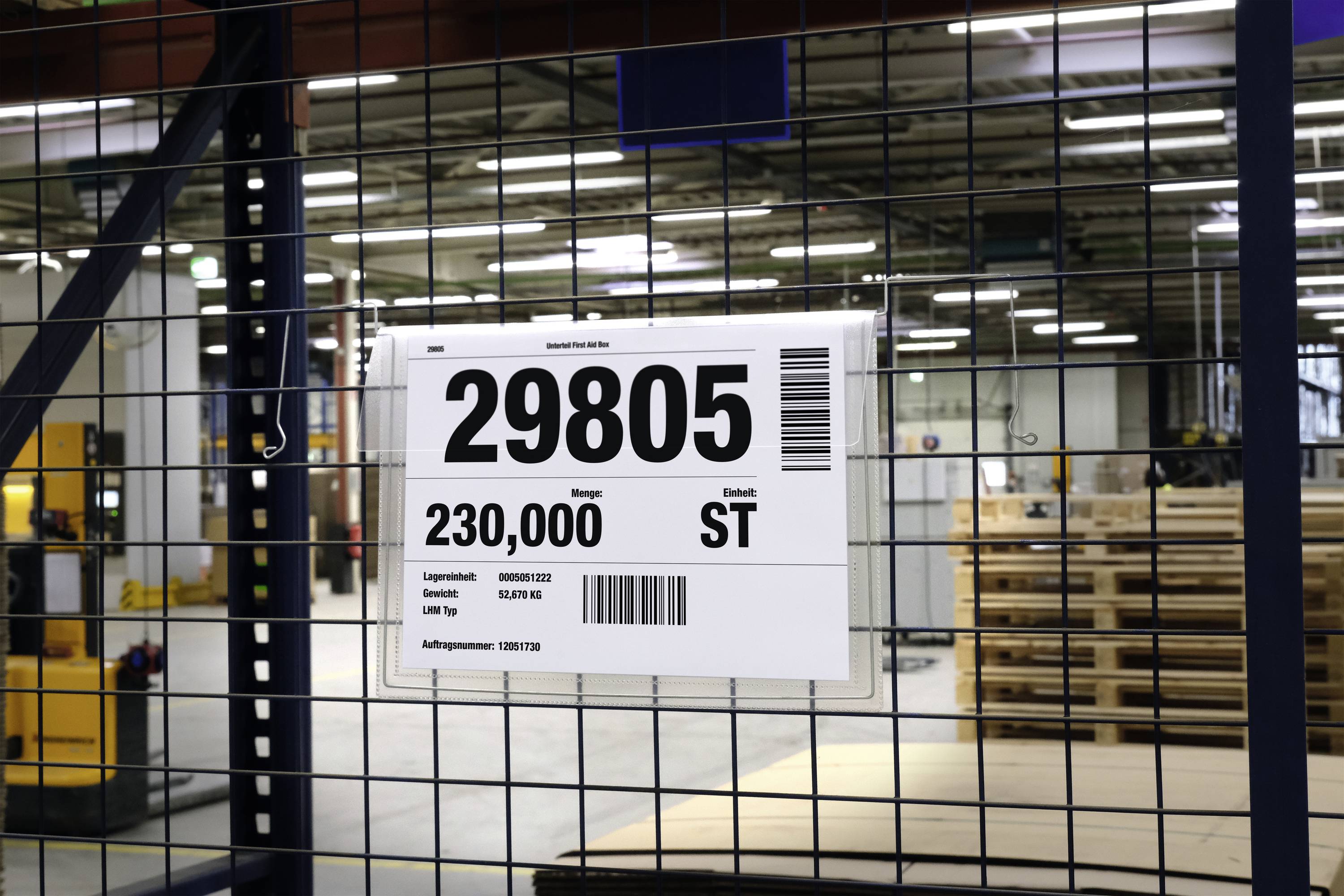 A sign displays '29805' with the details: Sheet metal 230,000 pcs, Storage location HAN1.002, Supplier UV 102, Item number 12997 F10. A warehouse is visible in the background.