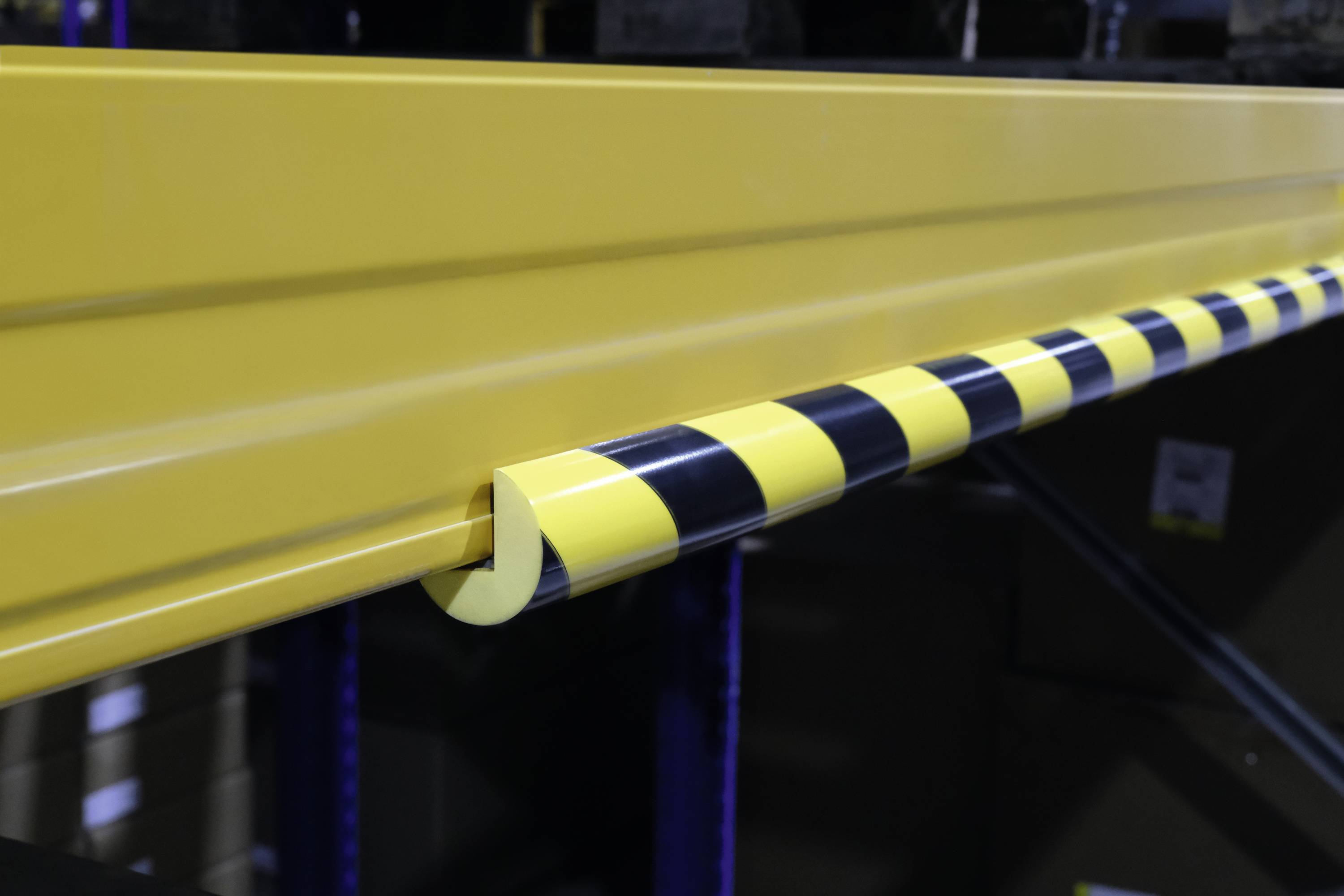 A yellow metal rail with a yellow and black striped impact protection padding, mounted on the edge to prevent accidents. Background blurred.