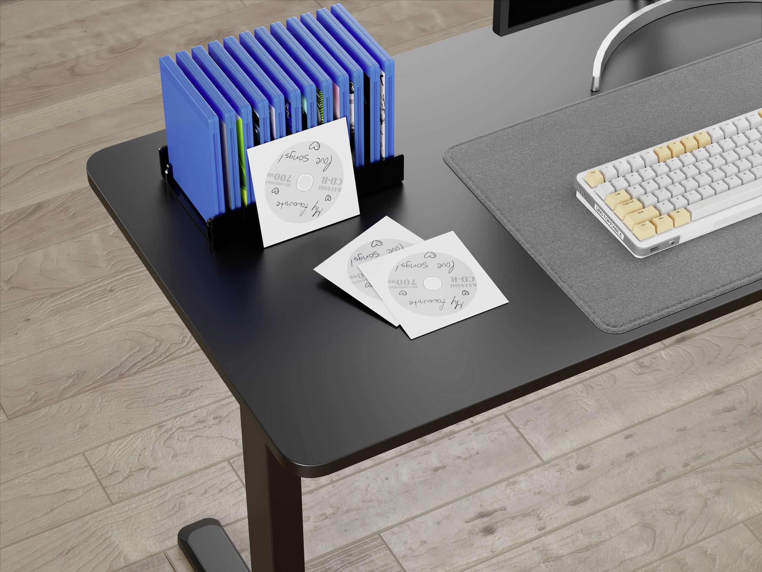 'A black desk with a keyboard, mouse mat, and a stack of blue DVD cases in a holder. Three DVDs with handwritten labels are spread out.'