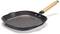 A black griddle pan with a ridged base and a wooden handle lies at an angle on a white surface.