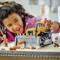 A child plays happily with a toy bulldozer on a table, surrounded by small toy figures and plastic parts.