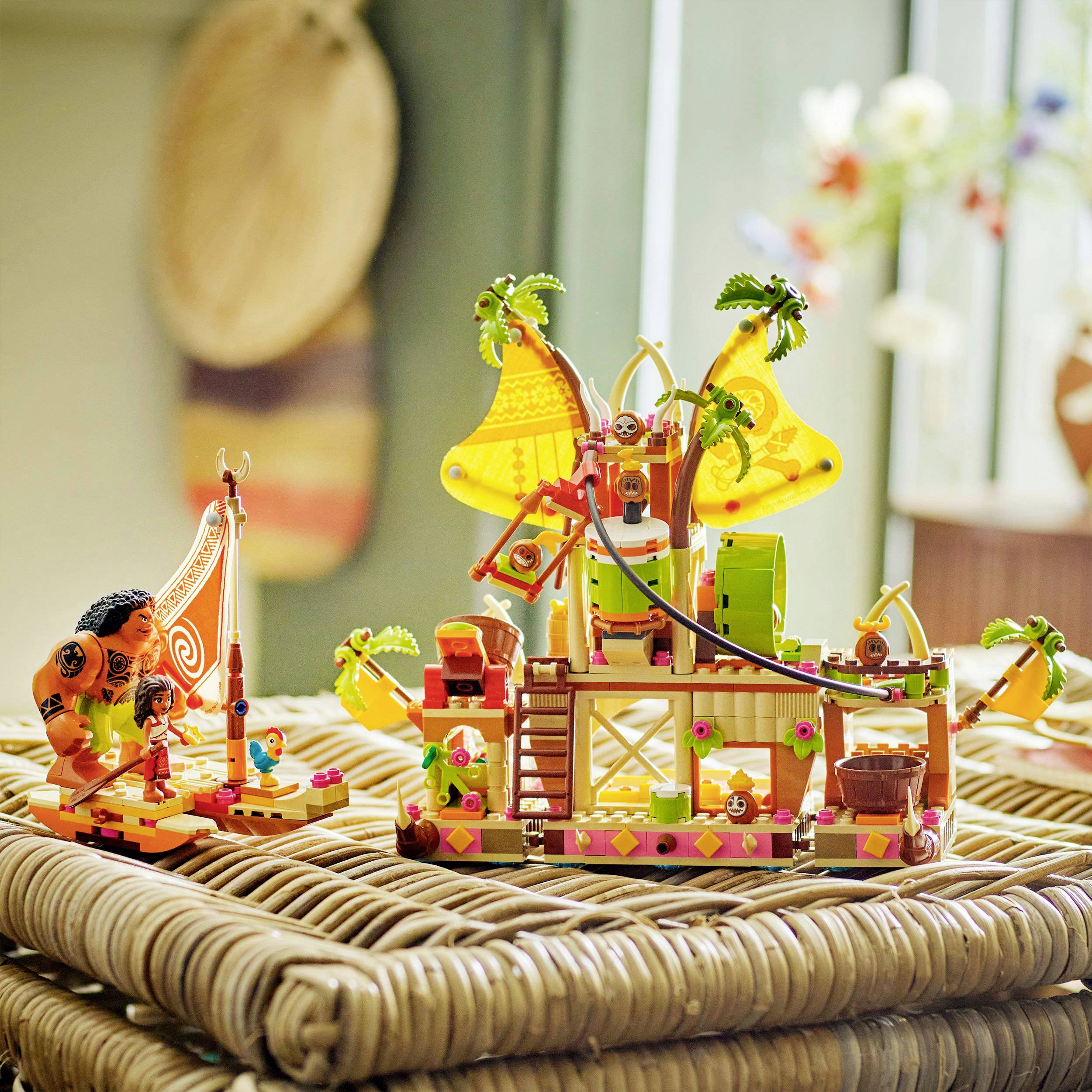 Toy adventure island made of colorful blocks with figures and palm trees on a wicker table, against a blurred, cozy background.