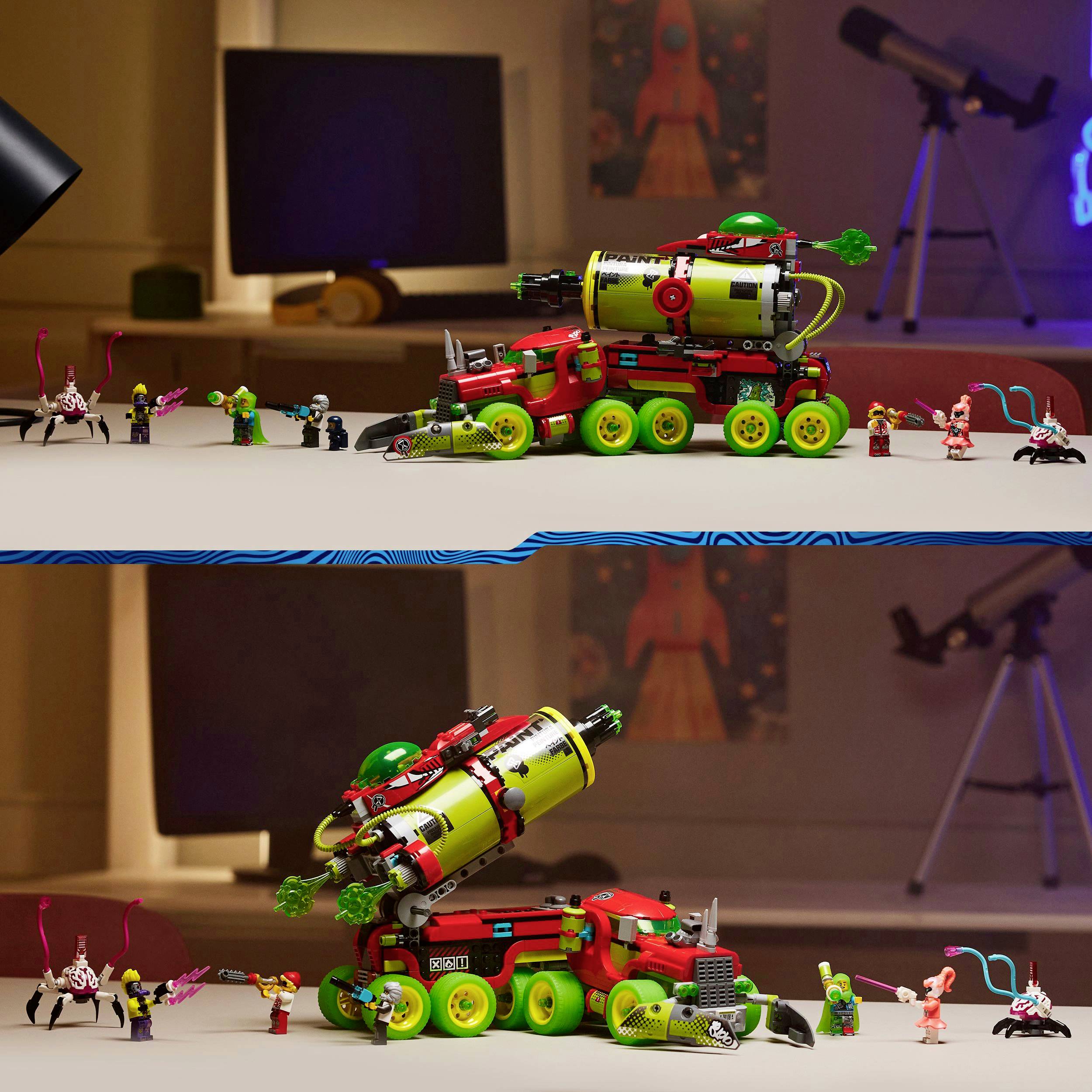 A red and green toy vehicle with a rocket launcher sits on a table, surrounded by small figures. Monitors can be seen in the background.