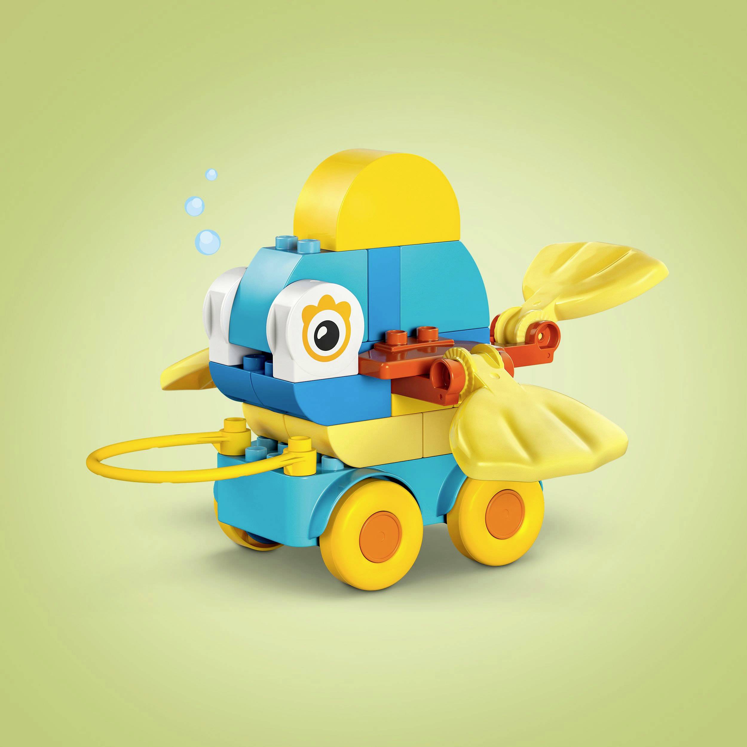 A colorful toy fish model made of building blocks with fins and wheels on a greenish background.