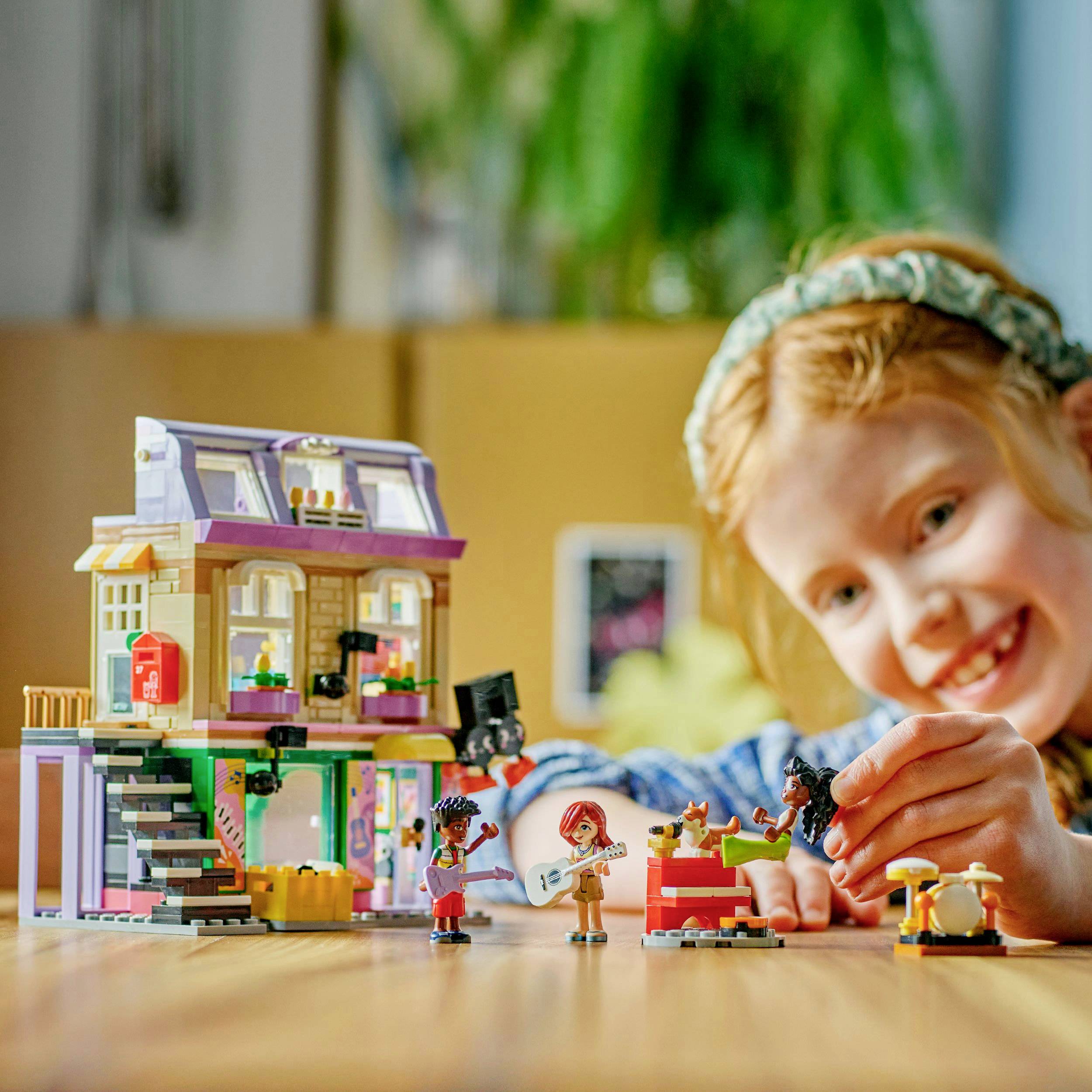 A child with red hair is playing with a dollhouse and several figures. The background is blurred.