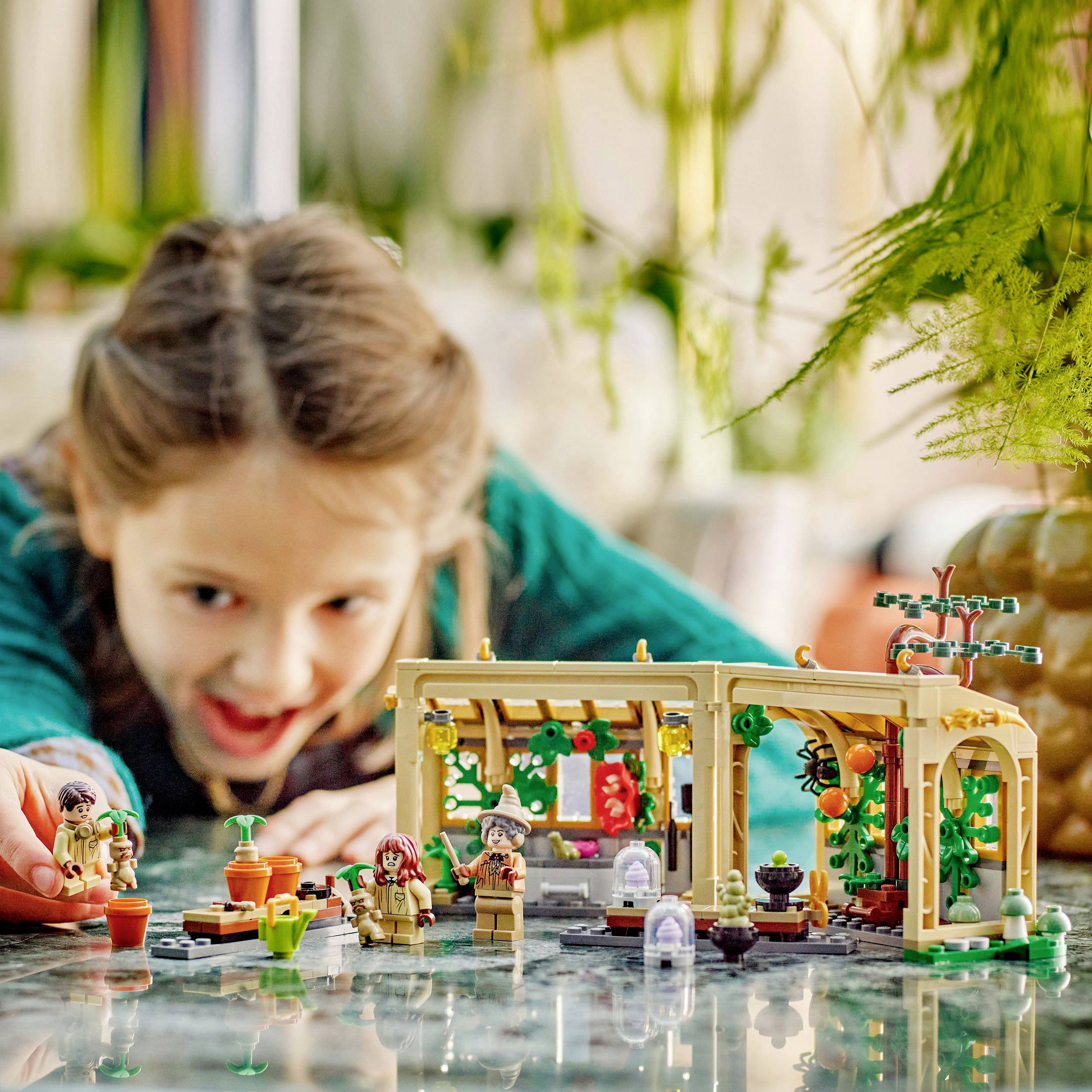 A girl is playing at the table with a plant Lego set. Various figures and plants made of Lego can be seen.