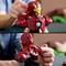 A person is holding a Lego model of a red and gold superhero suit. Hands are positioning parts of the model.