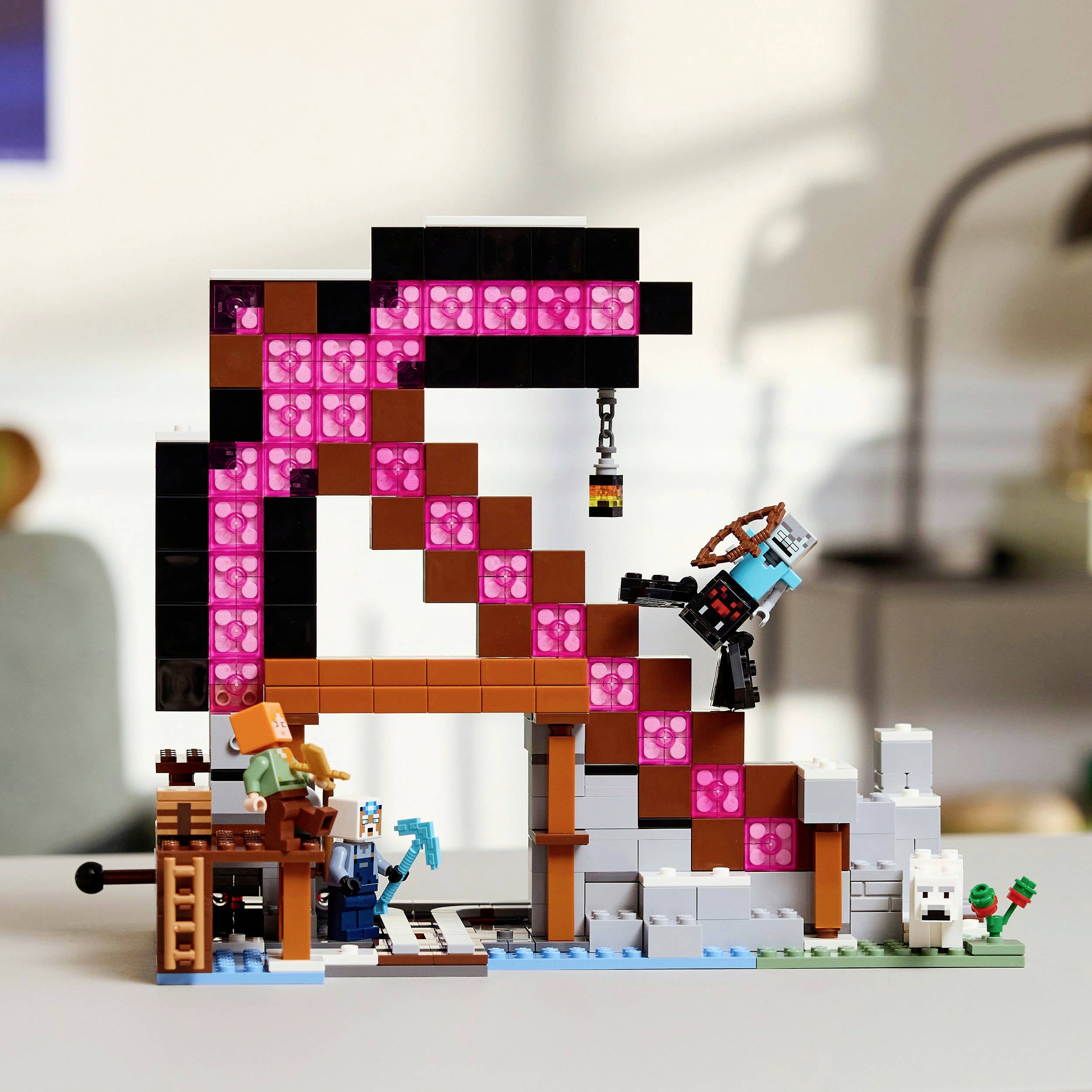 A Lego model with a Minecraft theme shows a large, pink pickaxe and miniature figures standing around a workbench. In the background is a desk.