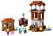 Building set made of Lego bricks with two buildings, figures and animals. One figure is riding on an animal, others are standing nearby.