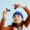 A child with a blue hat joyfully holds two action figures up in the air, one on a motorcycle and one with wings, against a blue background.