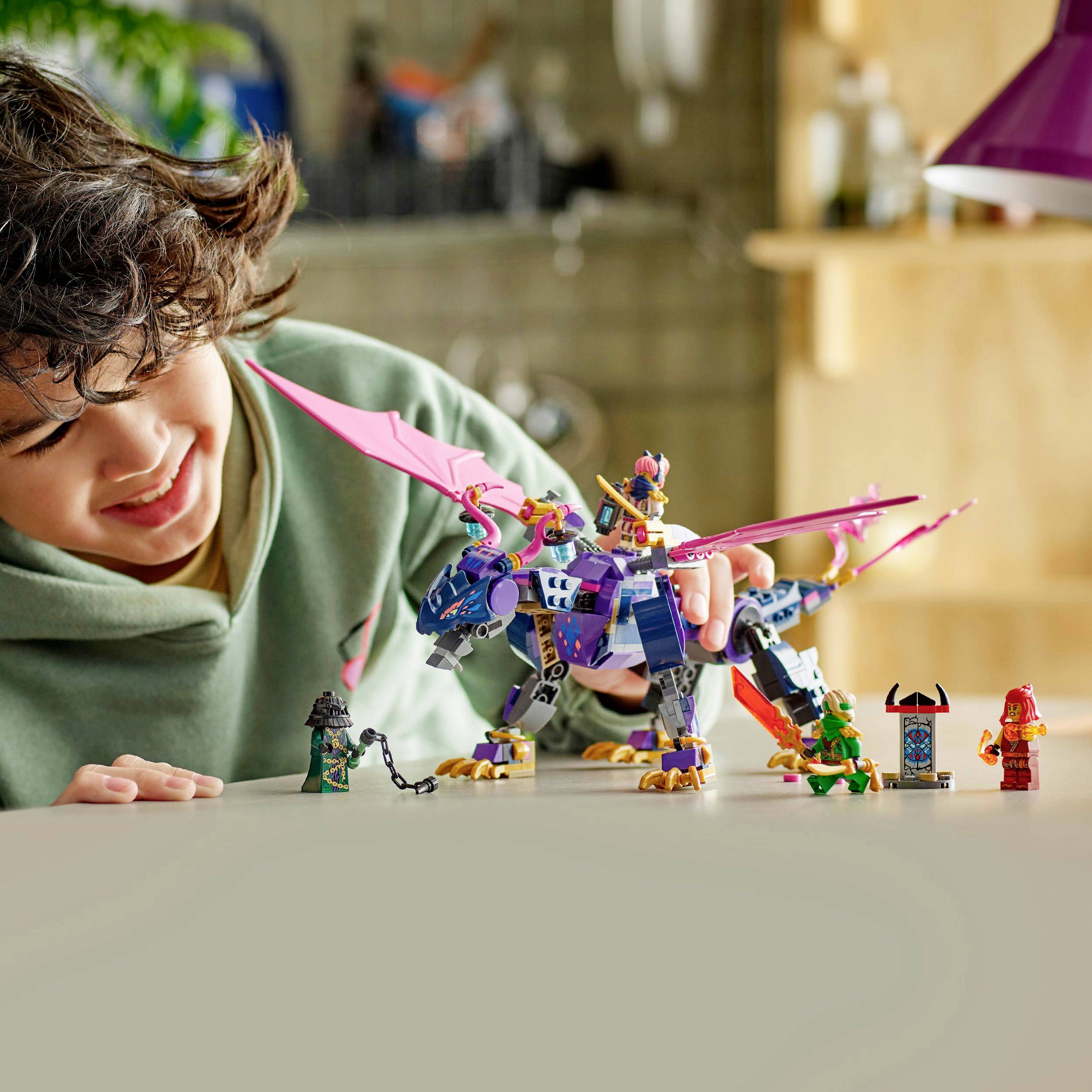 A child is playing with a colorful, buildable toy dragon and figures on a table. The dragon is purple with pink wings.