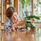 Boy plays enthusiastically with colorful robot models made from building blocks on a wooden table in a bright room with plants in the background.