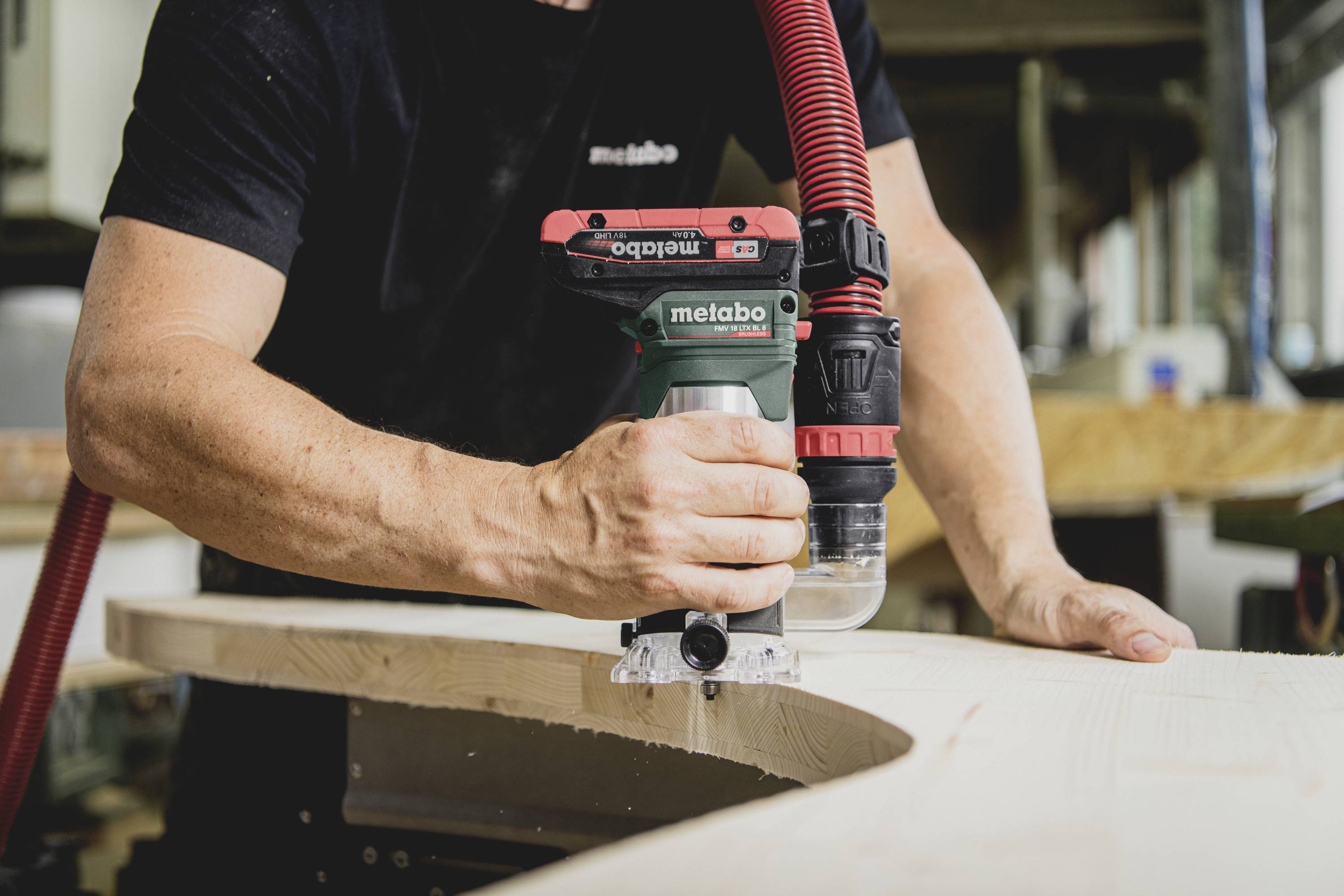 A person is operating a router to work with wood, shaping the edge of a wooden board in a workshop.
