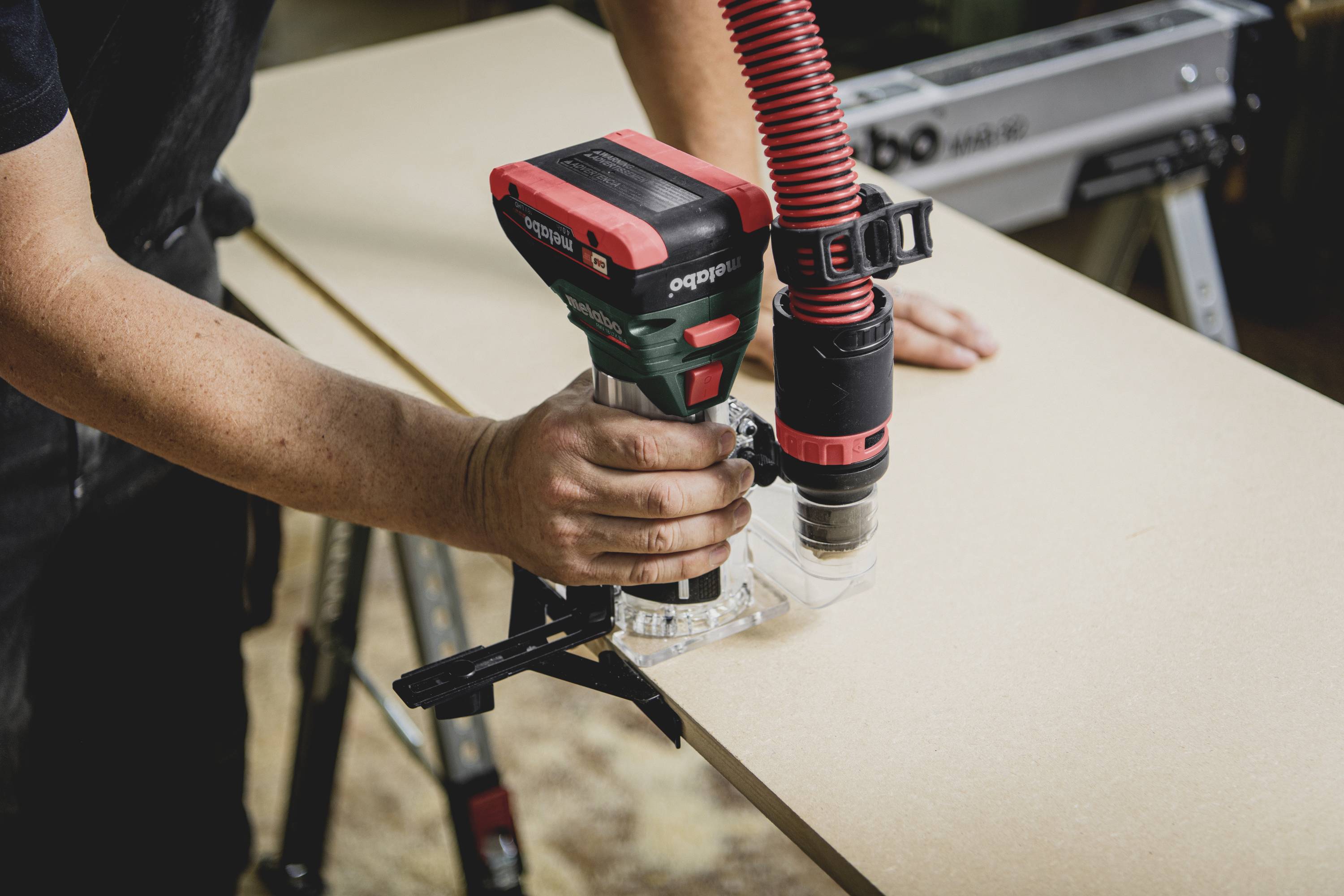 A person is drilling a hole in a wooden board using a drill. A red hose is attached to the drill.