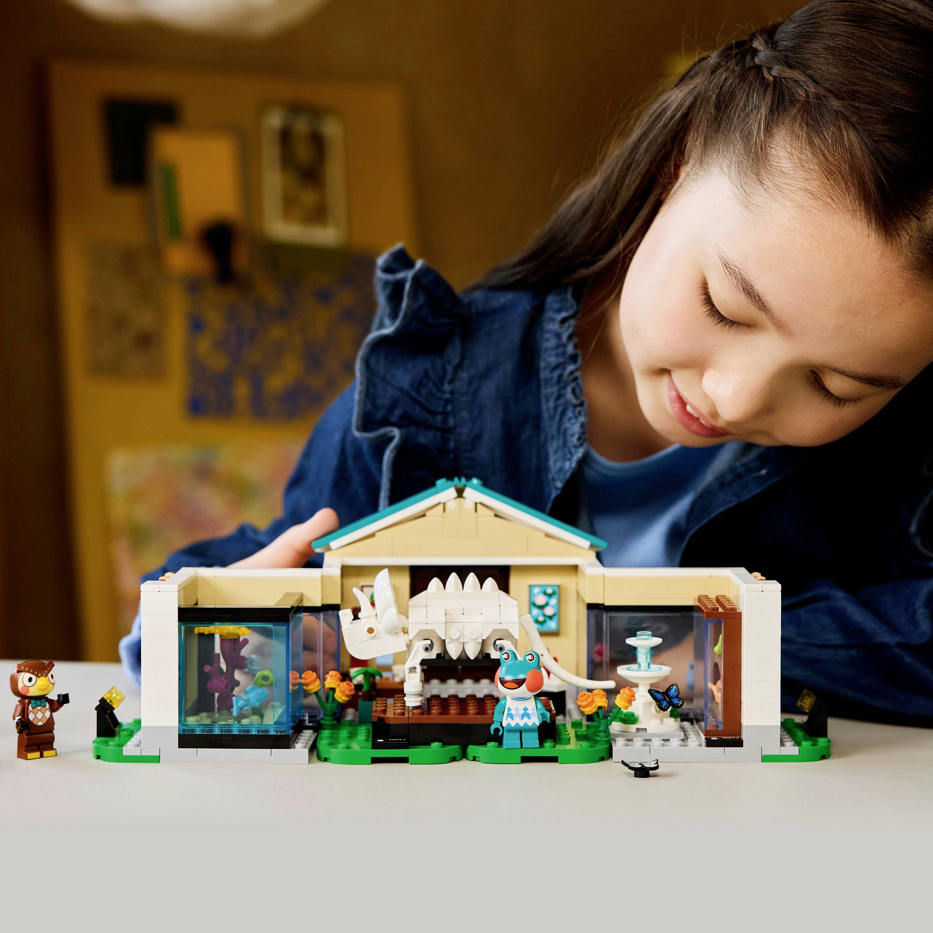 A child plays with a dinosaur-themed LEGO set on a table, featuring a small building and figures, in a warmly lit room.