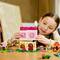 A child builds a colorful toy house with small figures on a wooden table, showcasing creativity and concentration.
