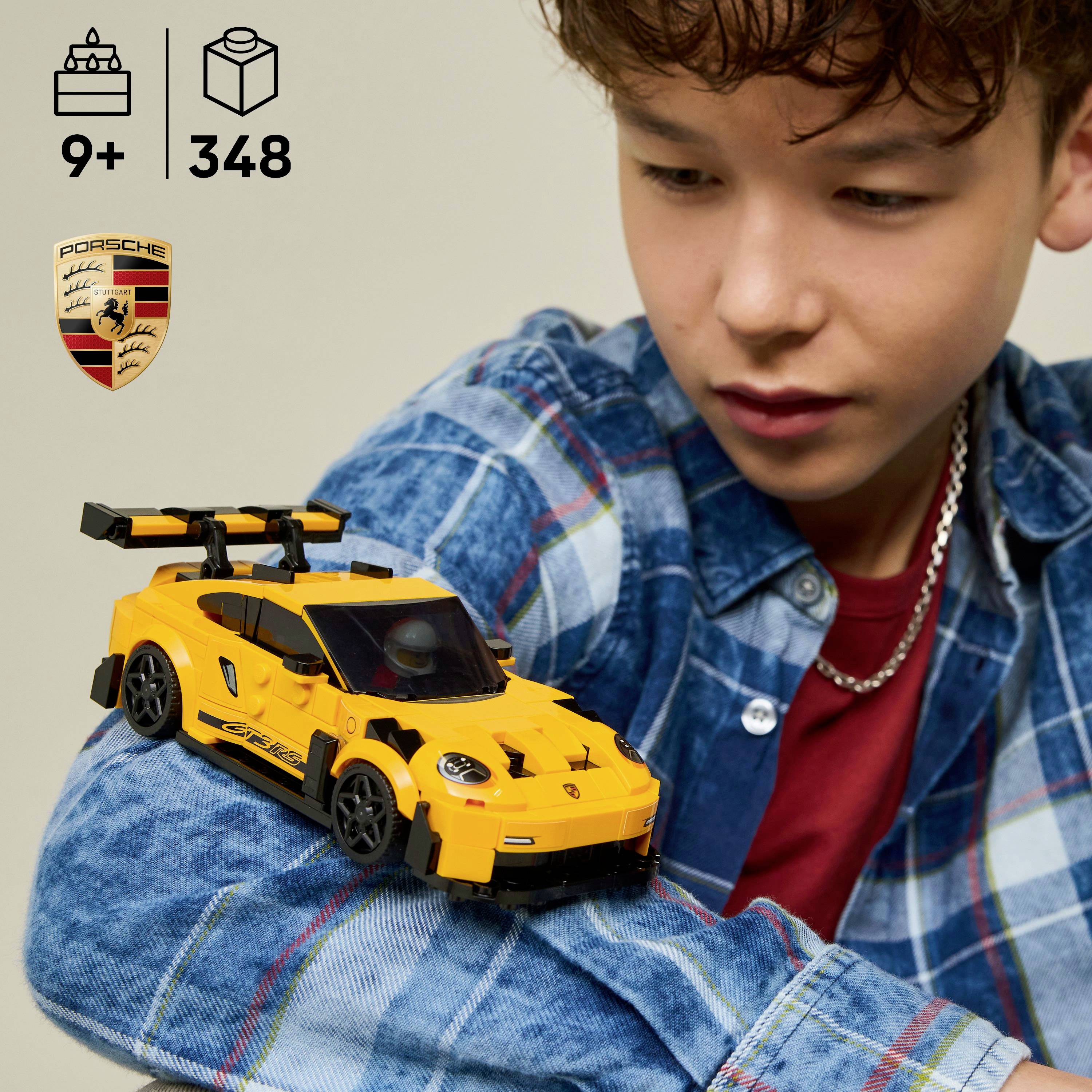 A child wearing a plaid shirt looks at a yellow toy sports car with a spoiler, logo, and racing decals, resting on their arm.