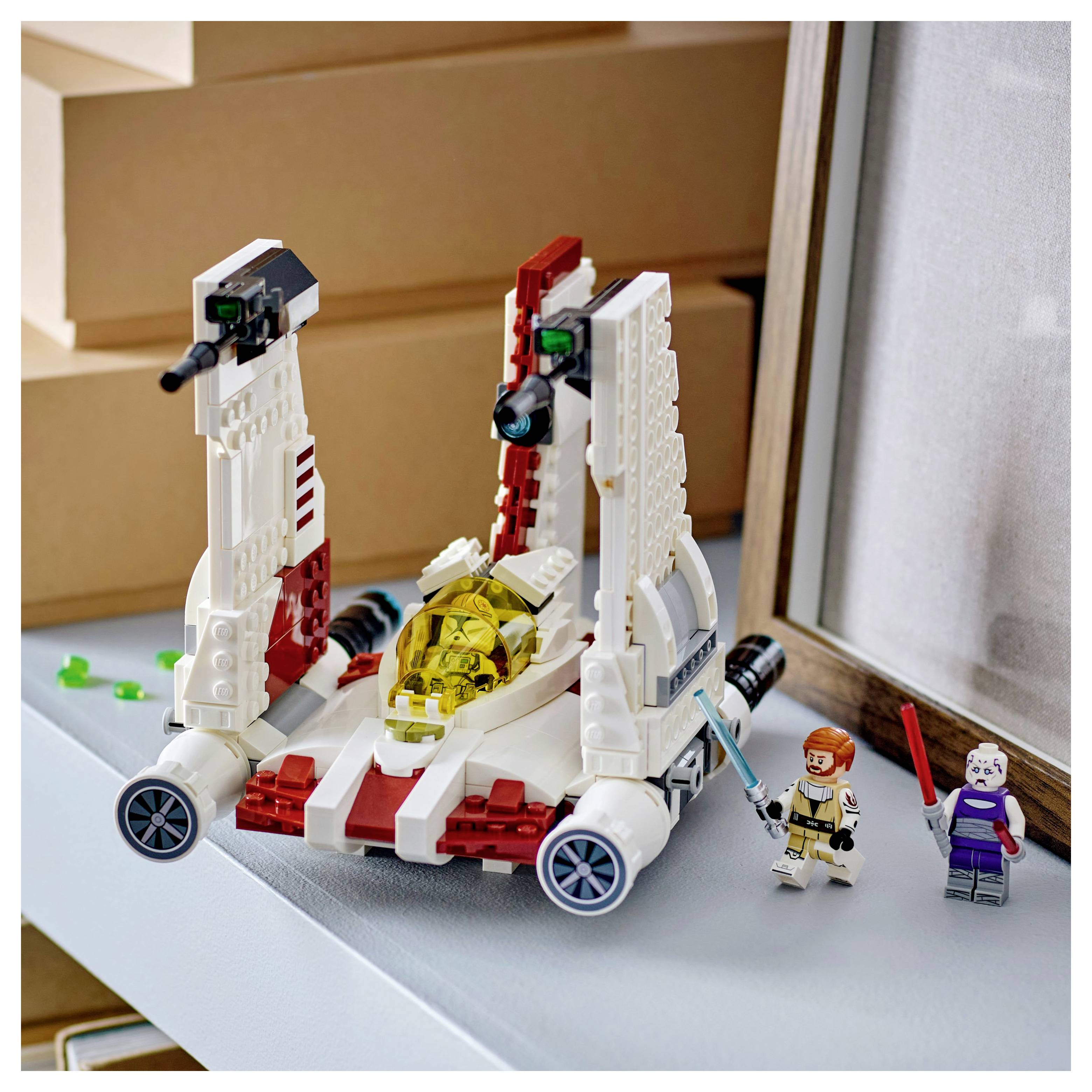 Toy spacecraft made of building blocks with two miniature figures holding swords. The scene is set on a shelf near a framed object.