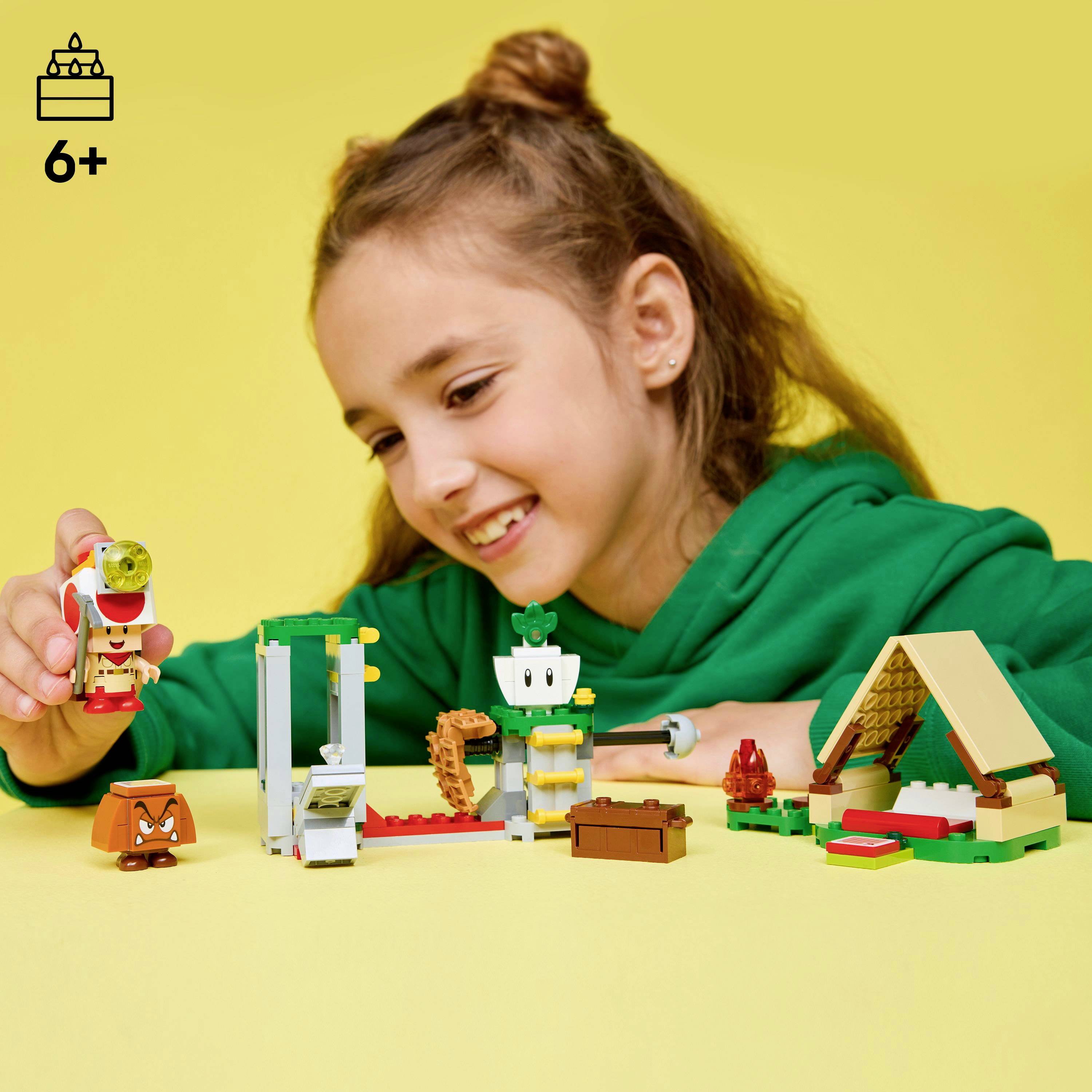 A child in a green sweater plays with a colorful construction toy set on a yellow table. The toy box indicates it's for ages 6 and up.