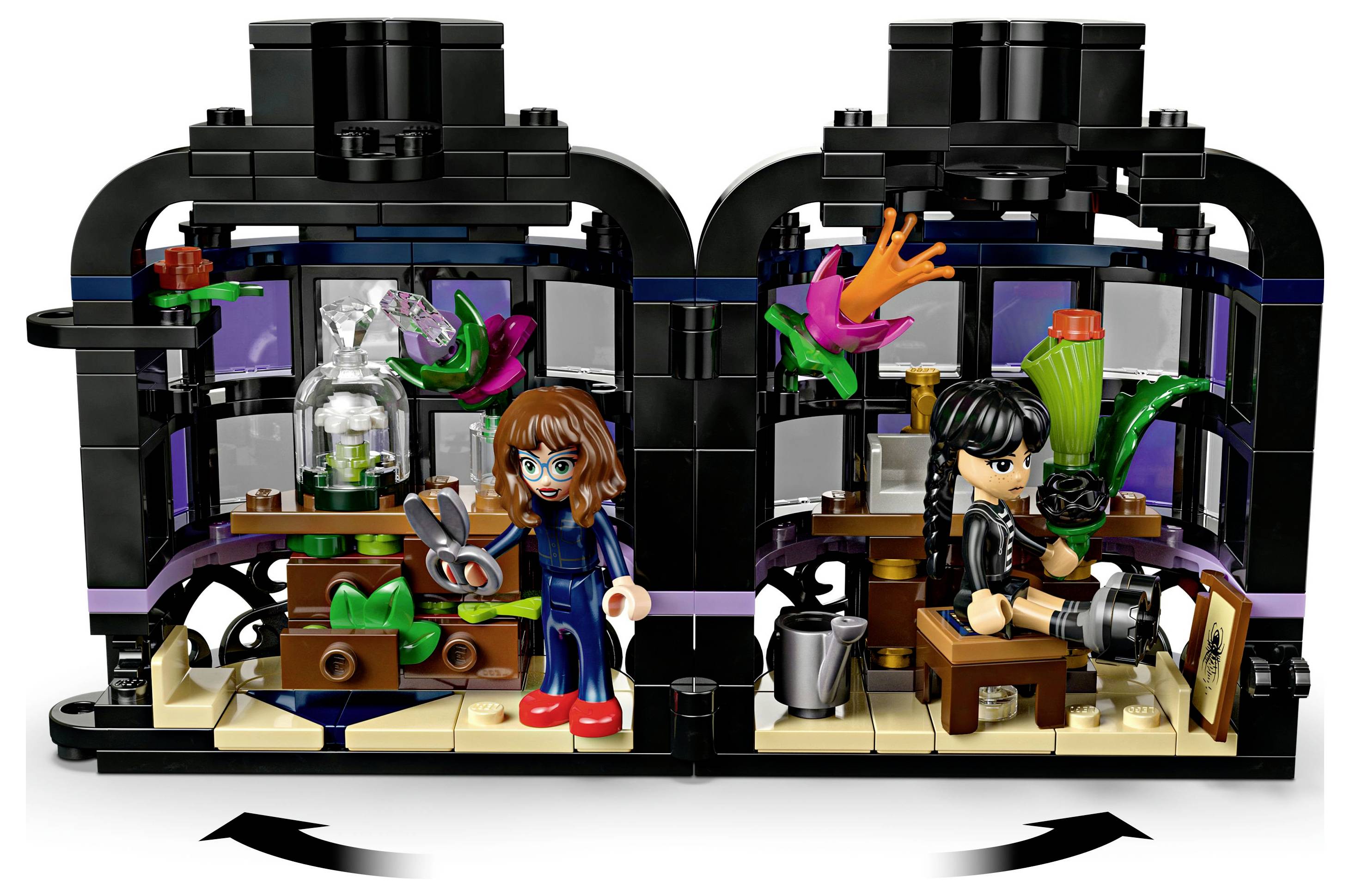 Two Lego figures in a greenhouse setting: one holds scissors near plants, the other sits with a camera. Various colorful plants surround them.