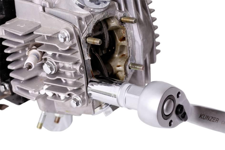 A motor with an open cylinder is being worked on with a torque wrench. Screw threads are visible in the background.