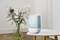A blue Ecomed air humidifier sits on a white table, with a vase of flowers in the background.