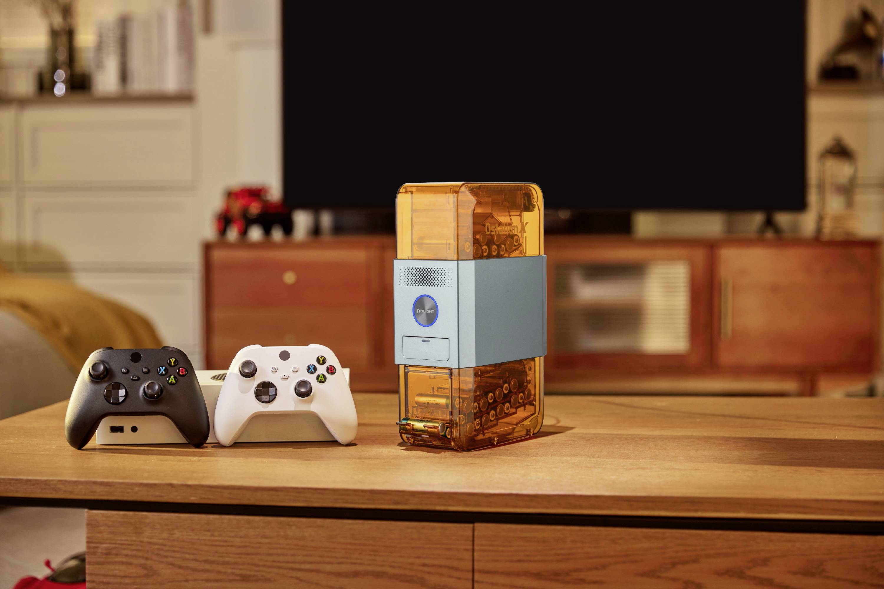 Two gaming controllers and a transparent orange router sit on a wooden table in front of a television in a living room.