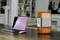 A laptop and an orange air purifier are placed on a table in a modern living room with a bookshelf in the background.