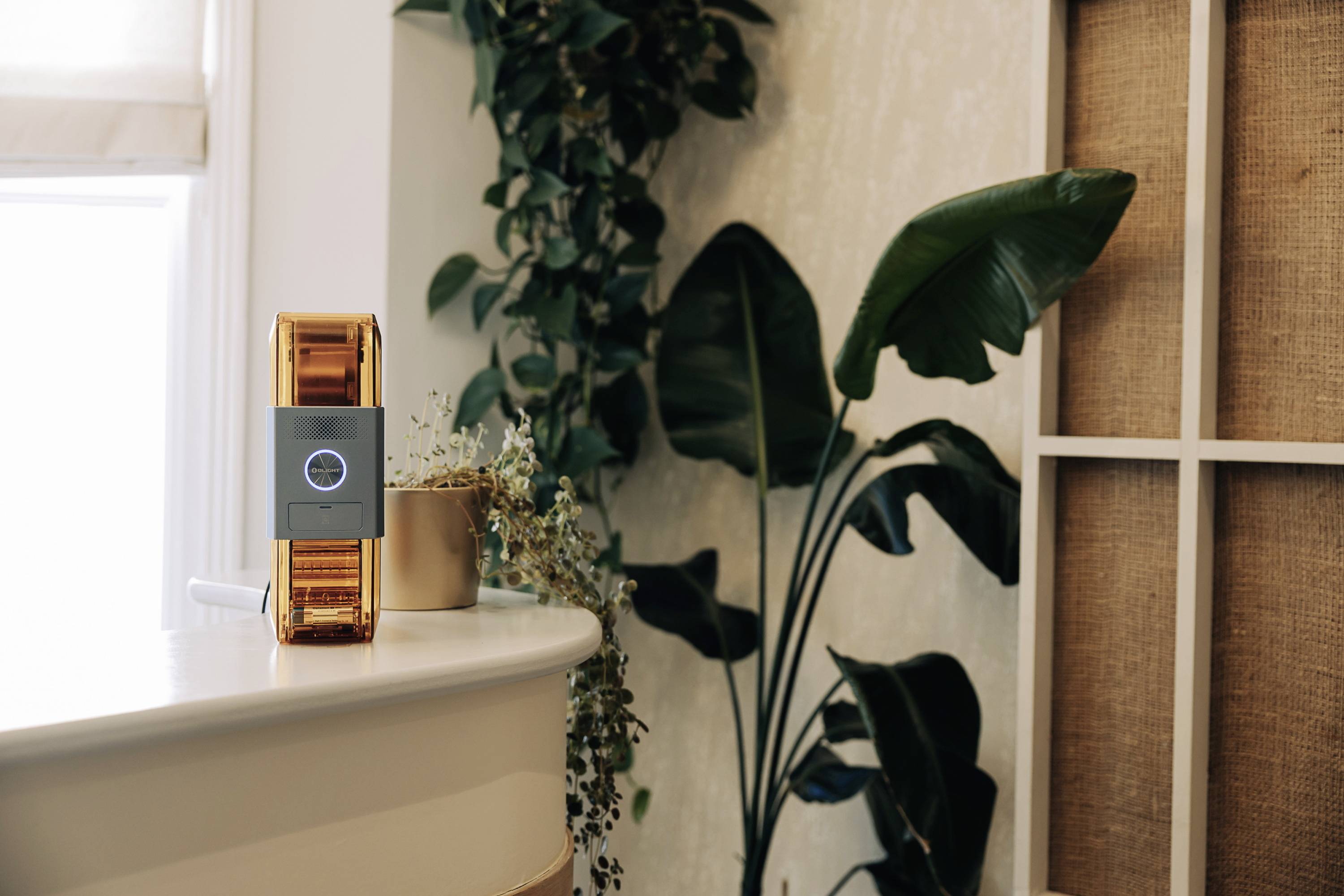 A modern air purifier on a table in a stylish living environment with plants in the background.