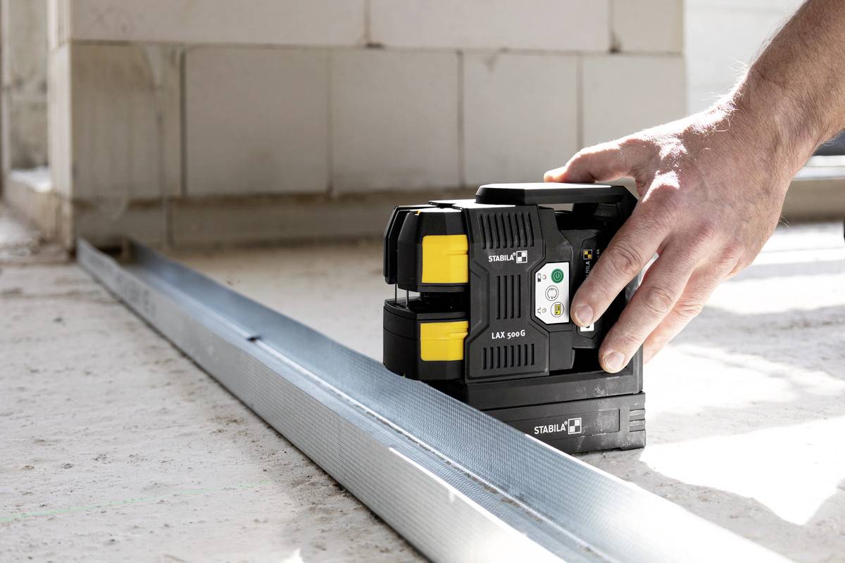 A hand is operating a laser level that is aligned on a metal ruler on a construction site.