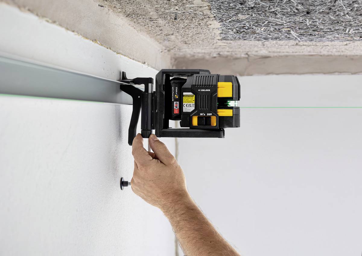 A hand adjusts a laser spirit level on a metal rail on the ceiling. The green laser line indicates the levelling.