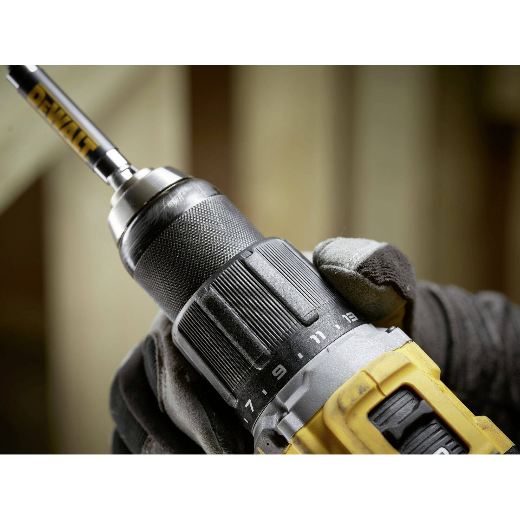A black and yellow drill is being held by a person wearing gloves. The focus is on the mounted drill bit.