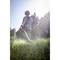 A person wearing protective clothing is mowing grass with a lawn strimmer in a sunny garden.