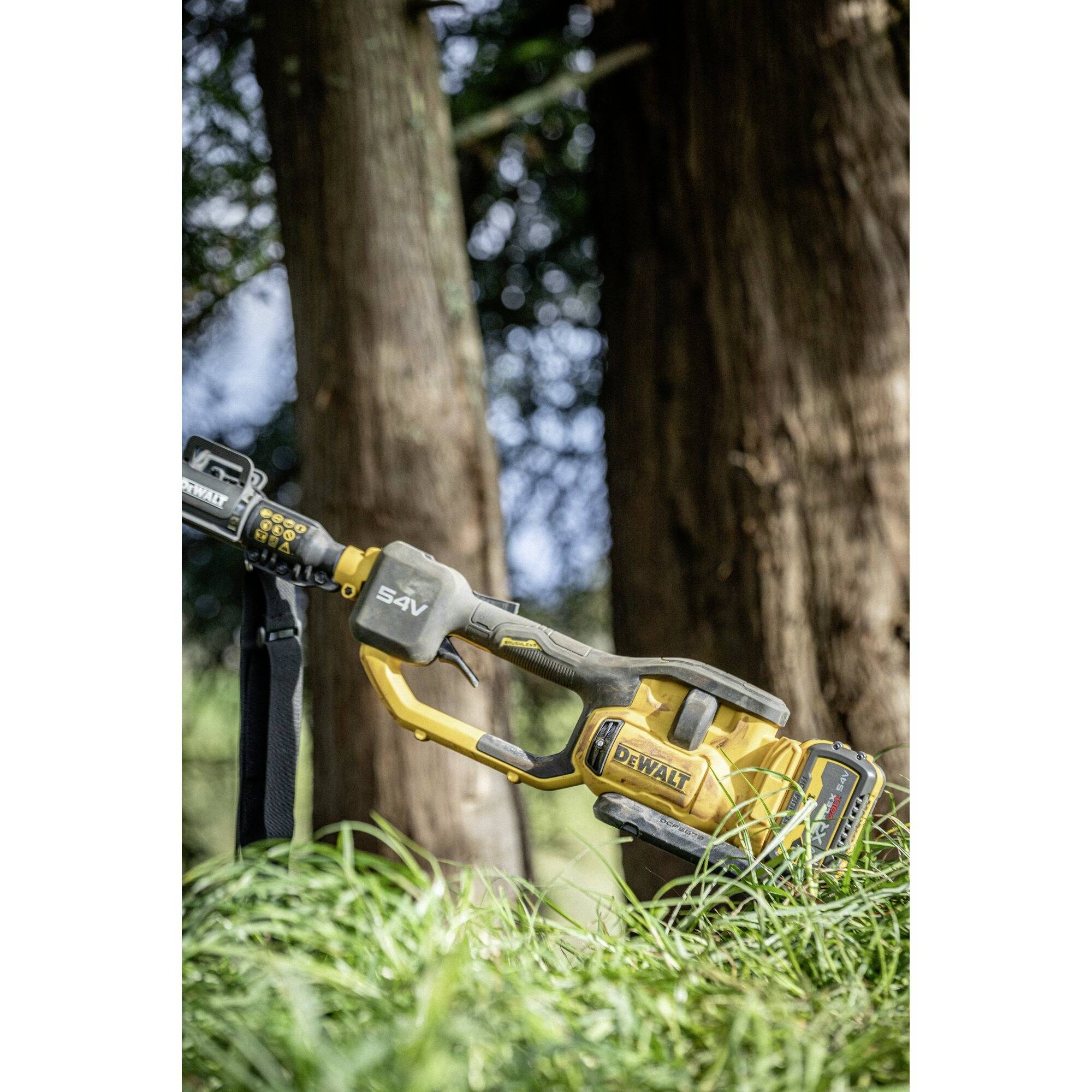 'Close-up of a yellow chainsaw in tall grass, with trees in the background. The chainsaw is prepared for use in the forest.'