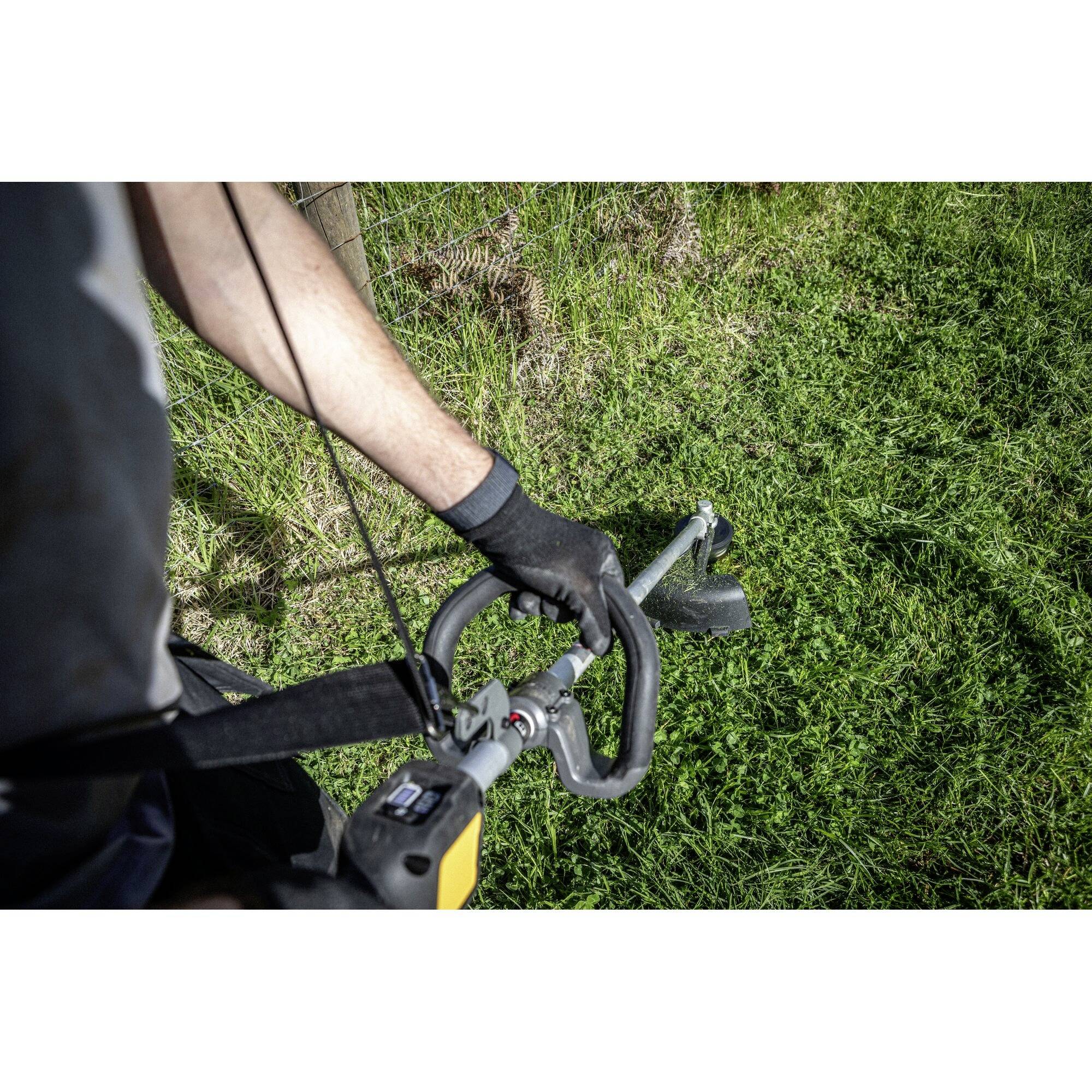 A person is mowing the grass with a lawn strimmer on a meadow. The person is wearing black gloves and gripping the strimmer firmly.