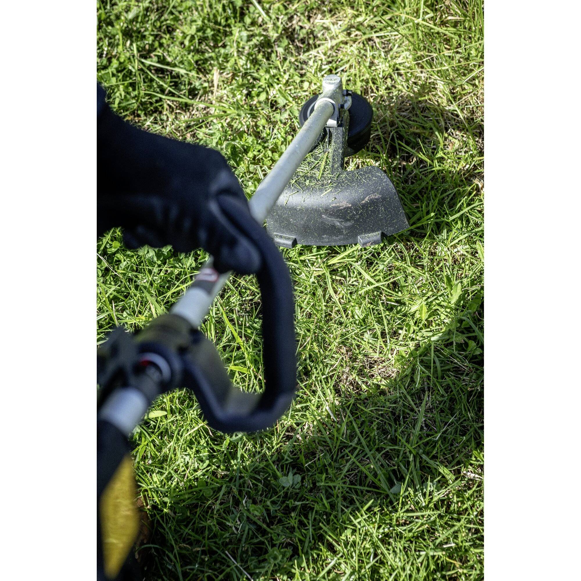 A person is using a strimmer to cut grass. The strimmer is being guided over a green lawn.