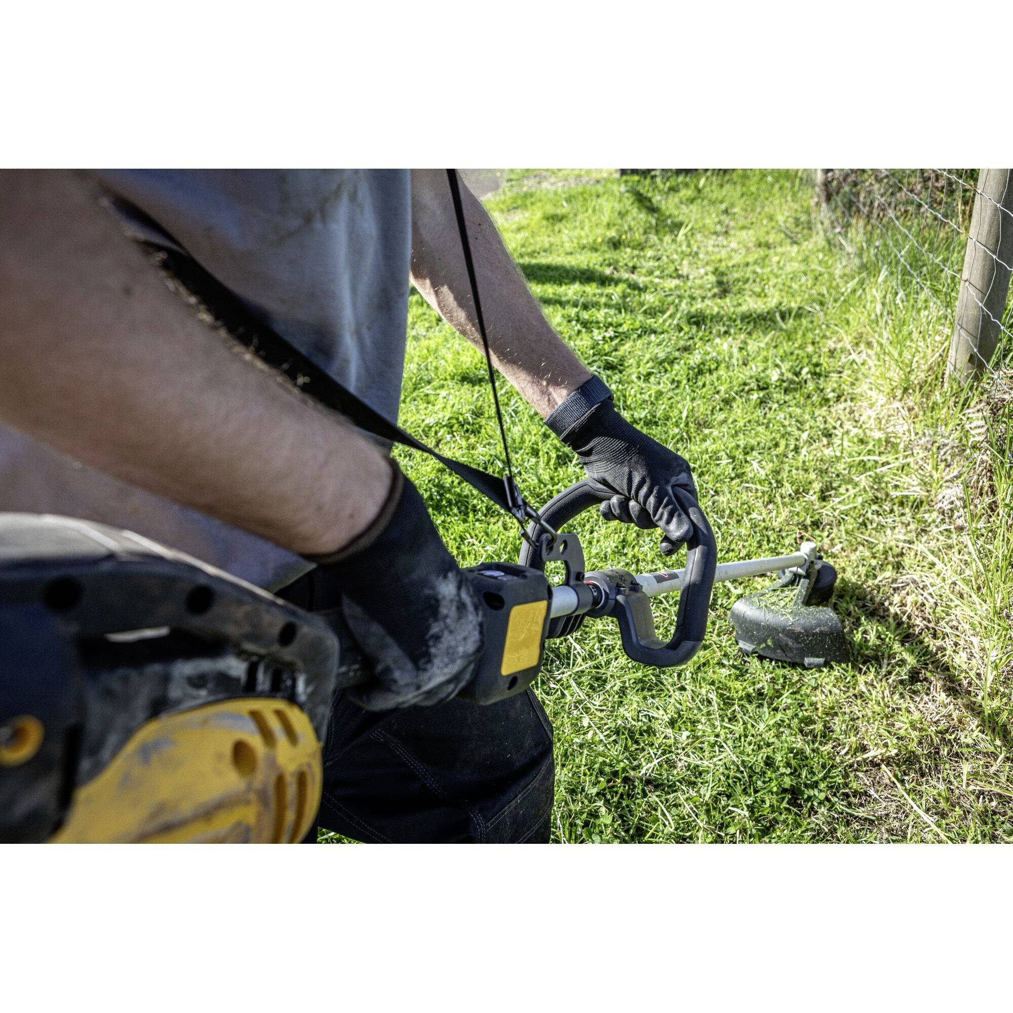 A person is operating a lawn trimmer to cut grass along the edge of a garden. They are wearing gloves and have a firm grip on the device.