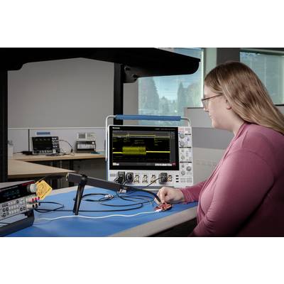 A person in a laboratory is examining an oscilloscope screen with data waveforms. Additional equipment is visible in the background.