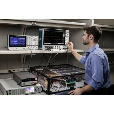 A man is operating test equipment on a laboratory bench, including oscilloscopes and a power supply, for analysing electronic circuits.
