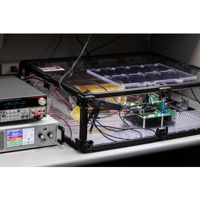A wired electronic testing device in a laboratory setting, next to a digital control unit.