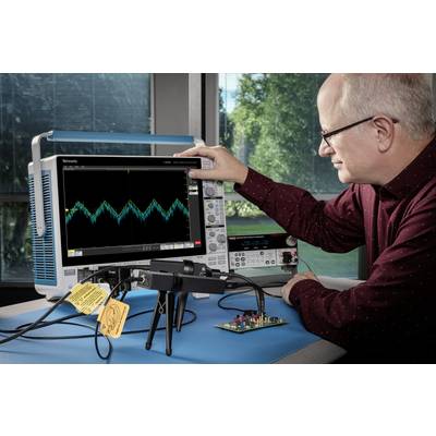 A man is working with an oscilloscope. Waveform graphics representing electronic signals are visible on the screen.