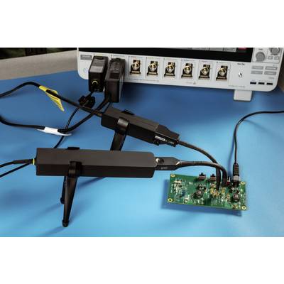 An oscilloscope on a table is connected to an electronic circuit. Cables and probes are attached to the circuits.