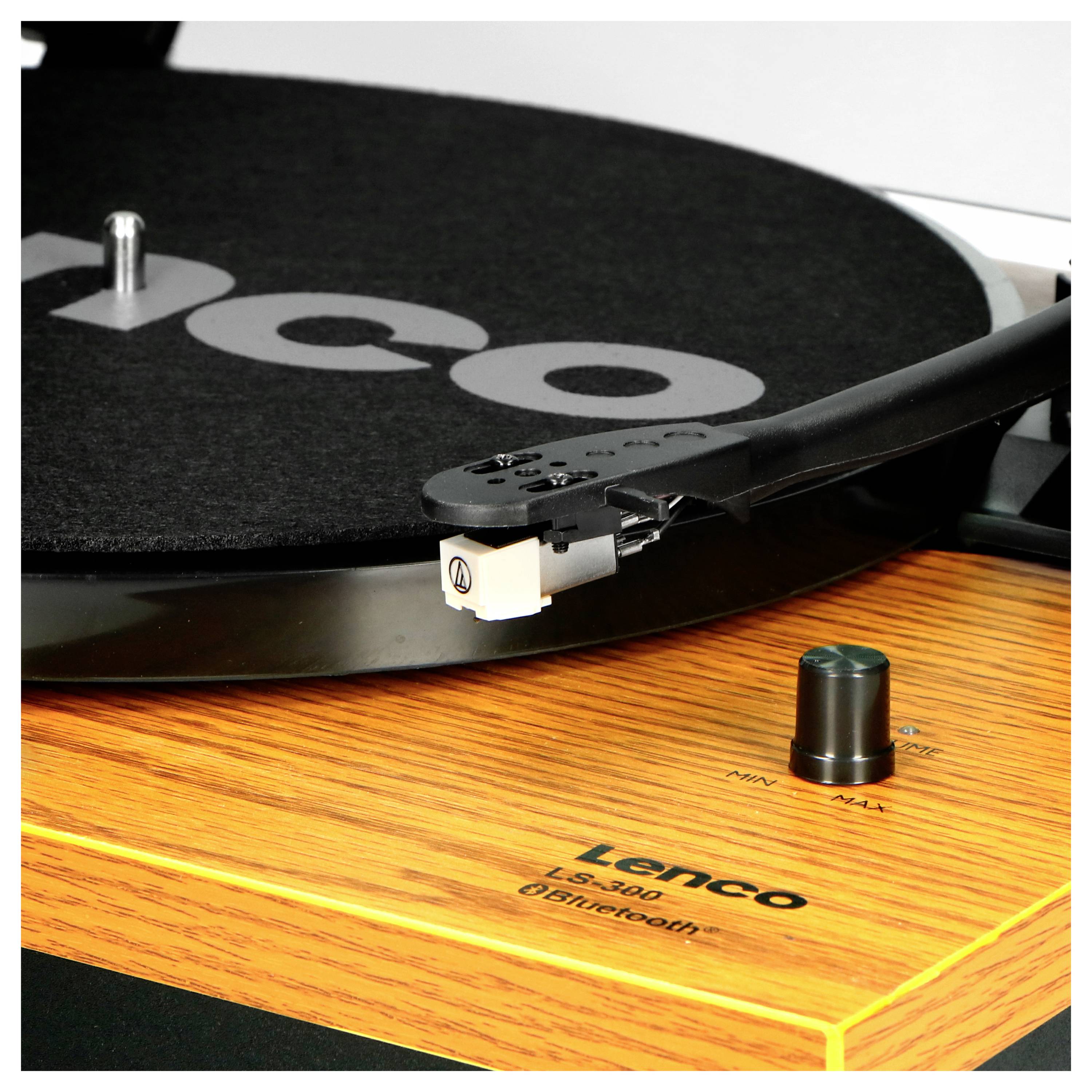 A Lenco turntable with a wood veneer finish. The tonearm is positioned on the record.