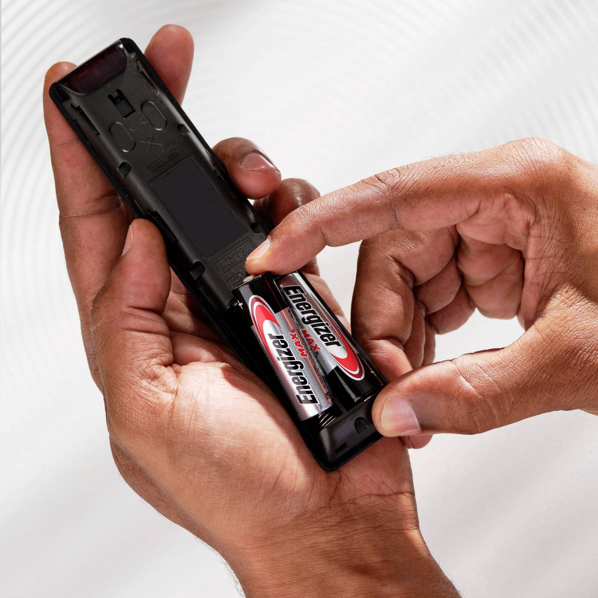 A hand holds a remote control and is inserting an 'Energizer' battery.