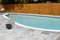 A backyard pool with clear blue water, surrounded by a stone patio. A wooden privacy fence is in the background. A filter pump is visible.
