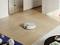 A robot vacuum cleaner is cleaning the wooden floor in a modern living room. Kitchen furniture can be seen in the background.