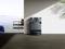 A robot vacuum with charging station stands in a minimalist room overlooking the sea and a terrace.