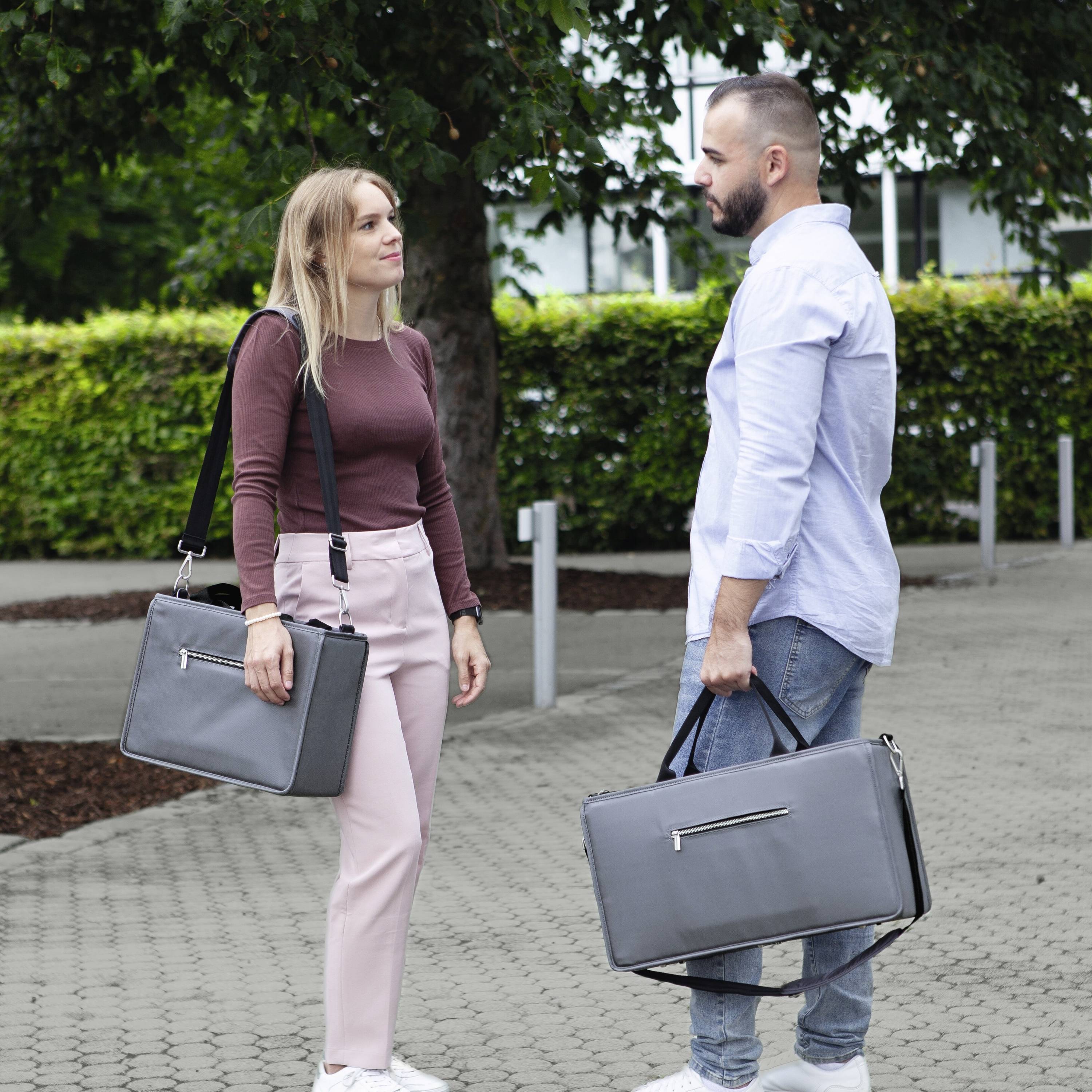 A man and a woman with briefcases are standing opposite each other on a paved path and are having a conversation.