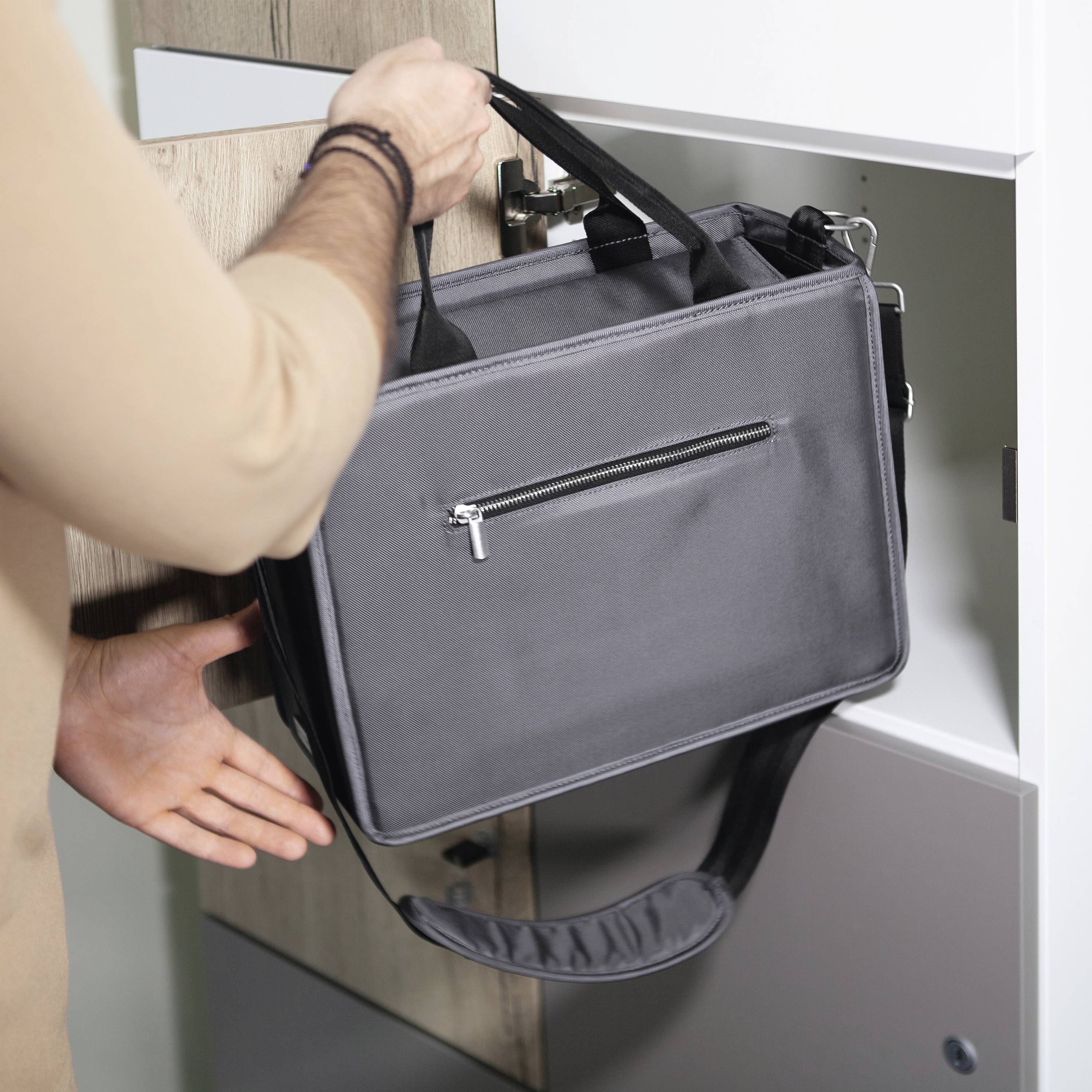 A person places a grey bag in a cupboard. The bag has a zip at the front. The scene appears organised and tidy.