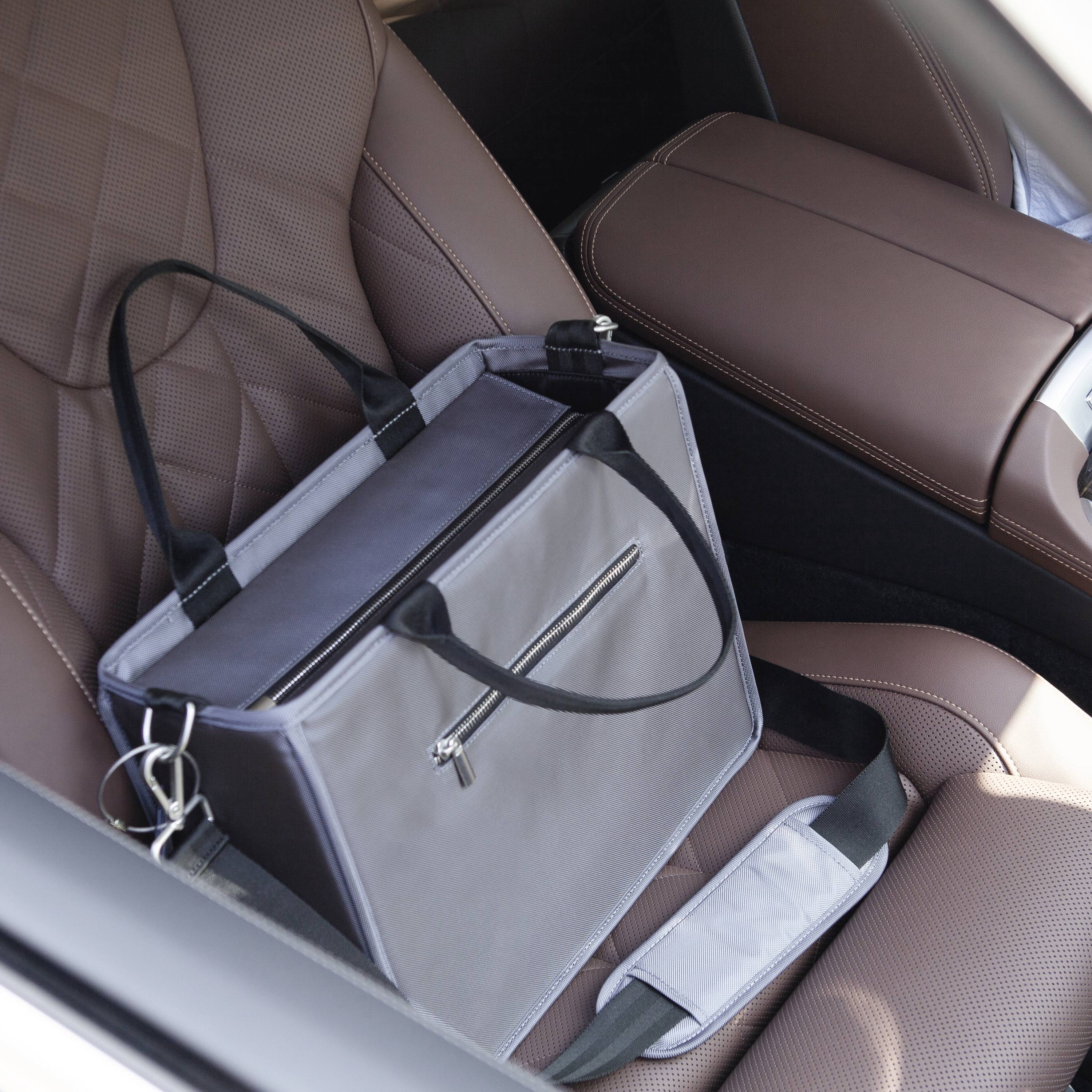 Grey shoulder bag with strap lies on a beige car seat. The bag has zips and a structured design.